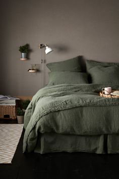 a bed with green linens and pillows in a dark colored room, next to a lamp