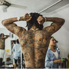 a man with tattoos on his back standing in front of other people and looking at the camera