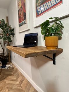 a laptop computer sitting on top of a wooden shelf next to a potted plant