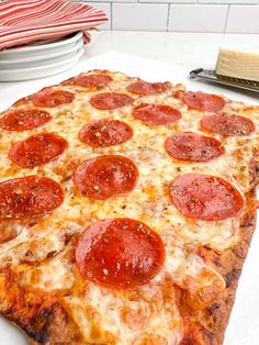 a large pepperoni pizza sitting on top of a table next to plates and utensils