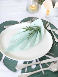 a white plate topped with green napkins next to silverware and candles on top of a table