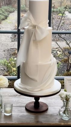 a three tiered white wedding cake sitting on top of a table next to a window