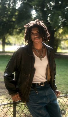 a man with dreadlocks leaning on a fence