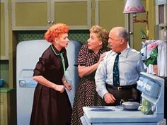 three people standing in front of an old fashioned stove and refrigerator, talking to each other