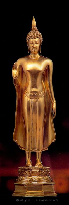 a golden buddha statue sitting on top of a wooden table in front of a black background