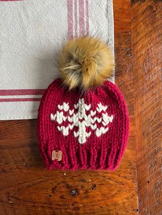 a knitted hat with a pom - pom sitting on top of a wooden table