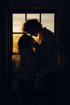 a man and woman kissing in front of a window with the sun shining through it