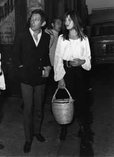 black and white photograph of people walking down the street with a man carrying a basket