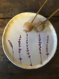 two wooden sticks sticking out of a white plate with lavender flowers on it and some rocks in the middle