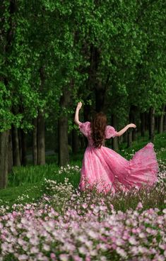 a woman in a pink dress is walking through the grass with her arms spread out