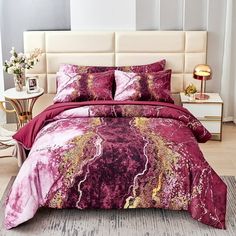 a bed covered in pink and gold comforter with pillows on top of it next to a night stand