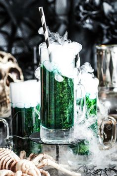 two mugs filled with green liquid sitting on top of a table next to skeleton bones