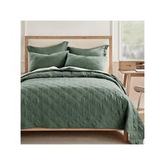 a bed with green comforter and pillows on it in front of a wooden headboard