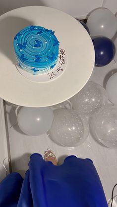 a blue and white cake sitting on top of a table surrounded by balloons, streamers and confetti