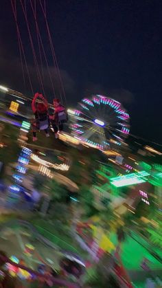 two people are parasailing in front of an amusement park with ferris wheel lights