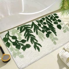 a bath mat with green leaves on it next to slippers and a pair of scissors