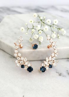 two pairs of blue and white crystal earrings sitting on top of a marble slab with flowers in the background