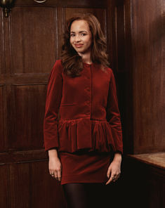 a woman in a red dress standing next to a wooden paneled wall and wearing black tights