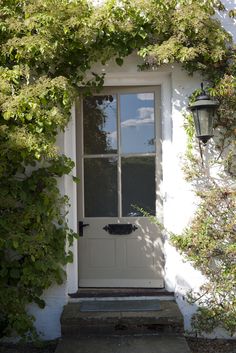 the front door to a white house with vines growing over it's side wall