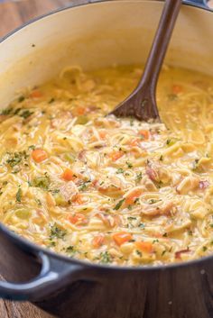 a wooden spoon in a pot filled with chicken noodle soup on top of a table