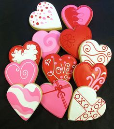 heart shaped cookies are arranged on a black tablecloth with red, pink and white designs