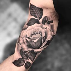 a black and white rose tattoo on the left arm, with leaves around it's edges