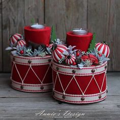 two red and white baskets with christmas decorations in them on a wooden table next to a wood wall