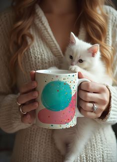 a woman holding a coffee mug with a white cat on it's arm and looking at the camera