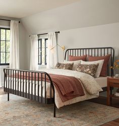 a bed sitting in a bedroom next to a window with curtains on the windowsill