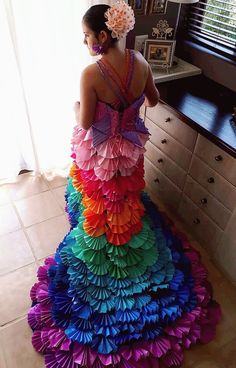 a woman standing in front of a window wearing a dress made out of paper flowers