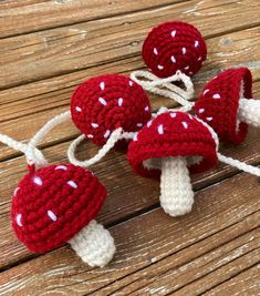 three crocheted mushrooms with white dots on them sitting on a wooden table next to string