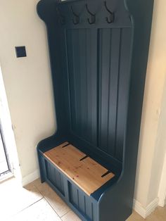 a blue bench with wooden seat and hooks on the back wall, next to a tiled floor