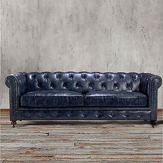 a blue leather couch sitting on top of a hard wood floor next to a wall