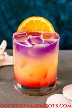 an orange and purple drink sitting on top of a table next to some sea shells