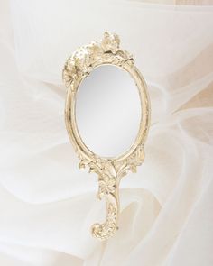 an ornate gold framed mirror on a white fabric background with the reflection of flowers in it