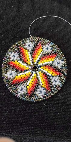 a colorful beaded ornament hanging on a black piece of cloth with thread