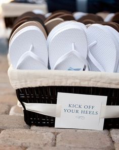 a basket filled with white flip flops sitting on top of a brick floor next to a sign that says kick off your heels