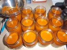 many jars filled with orange colored liquid sitting on a counter next to a metal bowl