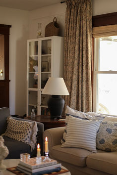 a living room filled with furniture and a lamp on top of a coffee table in front of a window