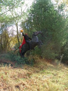 a man riding on the back of a black horse through a lush green forest filled with trees