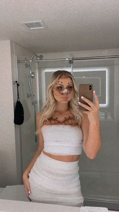 a woman taking a selfie in a bathroom mirror with her face painted like a cat