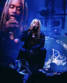 a man with dreadlocks sitting in front of a microphone on stage at a concert