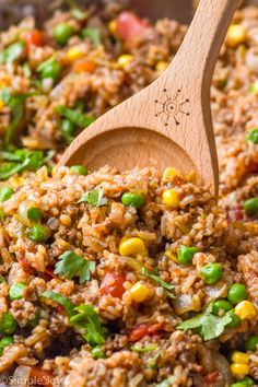 a wooden spoon stirring rice and vegetables in a skillet