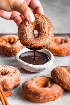 someone dipping chocolate into doughnuts on a tray