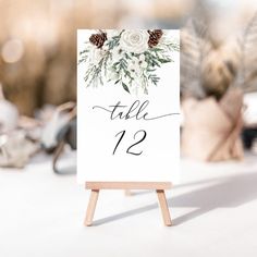 a table sign with flowers and pine cones on it