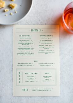 a menu sitting on top of a white table next to a glass of orange juice