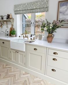 a kitchen with wooden floors and white cabinets, an open window over the sink is decorated with flowers