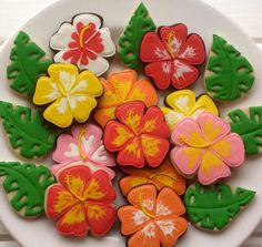 decorated cookies on a white plate with green leaves and flower decorations in the middle, sitting on a table