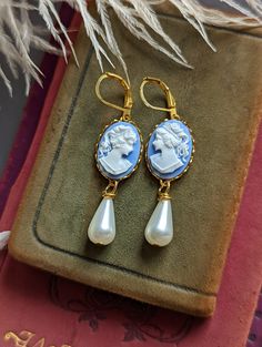 "Absolutely lovely, these peach cameo earrings are perfect for a Gothic or Historical period wedding! They would make an excellent gift for anyone that loves vintage-style jewelry. Featuring golden brass lace-edged bezel settings mounted with blue and white portrait cameos. Adorned with an elegant, teardrop shaped ivory glass pearl.  *Please note: the settings sometimes may have random designs on the back, this is common from processing and not noticeable while wearing. Size: Suspended by hook e Elegant Cameo Earrings, Elegant Round Cameo Earrings, Cameo Drop Earrings For Formal Occasions, Classic Cameo Earrings, Classic Cameo Earrings Gift, Elegant Cameo Clip-on Earrings Gift, Elegant Cameo Earrings As Gift, Elegant Cameo Earrings For Gift, Cameo Drop Earrings Jewelry Gift