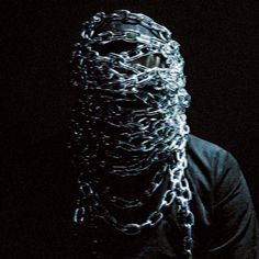 a man with chains on his face and hands in the dark, wearing a black shirt